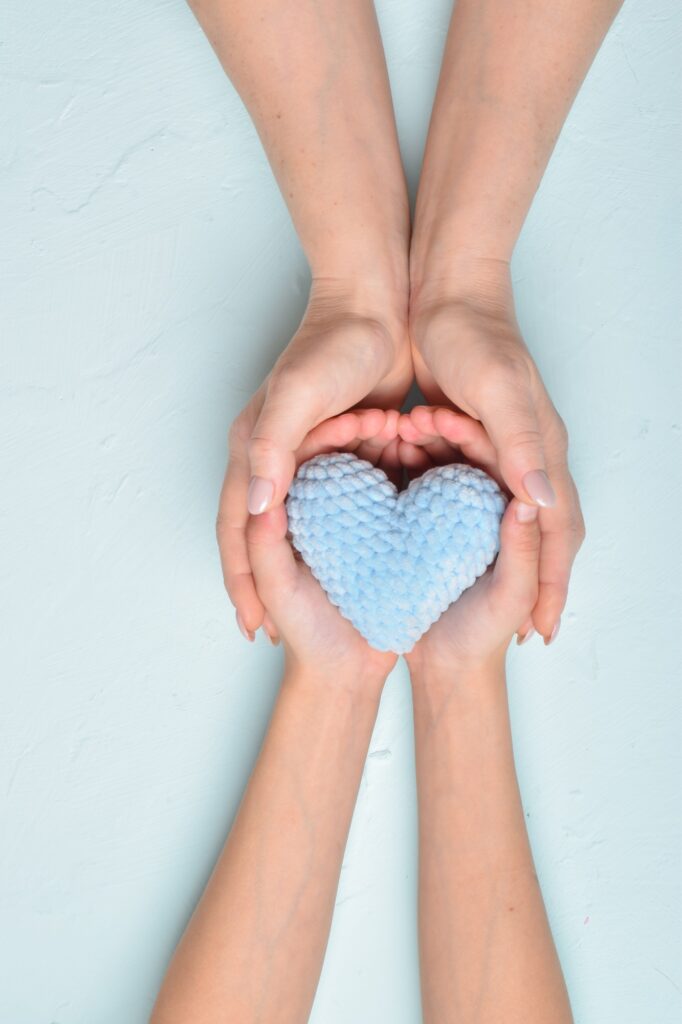 The baby passes the blue knitted heart into his mother's hands. Softness
